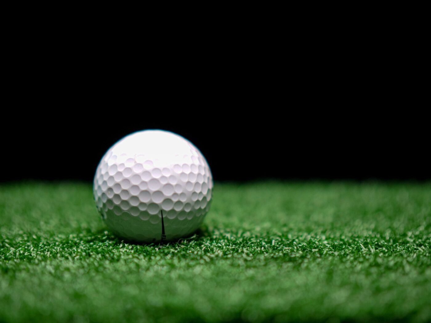 A close-up image of a white golf ball with dimples, placed on green artificial turf. The background is dark, making the golf ball and the green turf stand out prominently. Ideal for anyone considering backyard putting green installation, as seen in Tucson Artificial Grass setups in Tucson AZ.